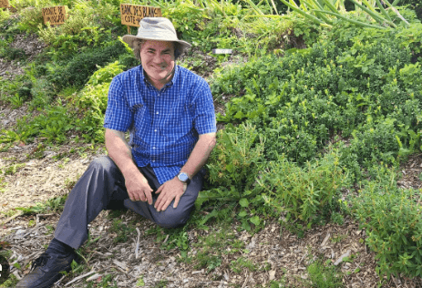 Homme portant une chemise bleu royale et un chapeau Tilley est assis dans le jardin de la ferme.