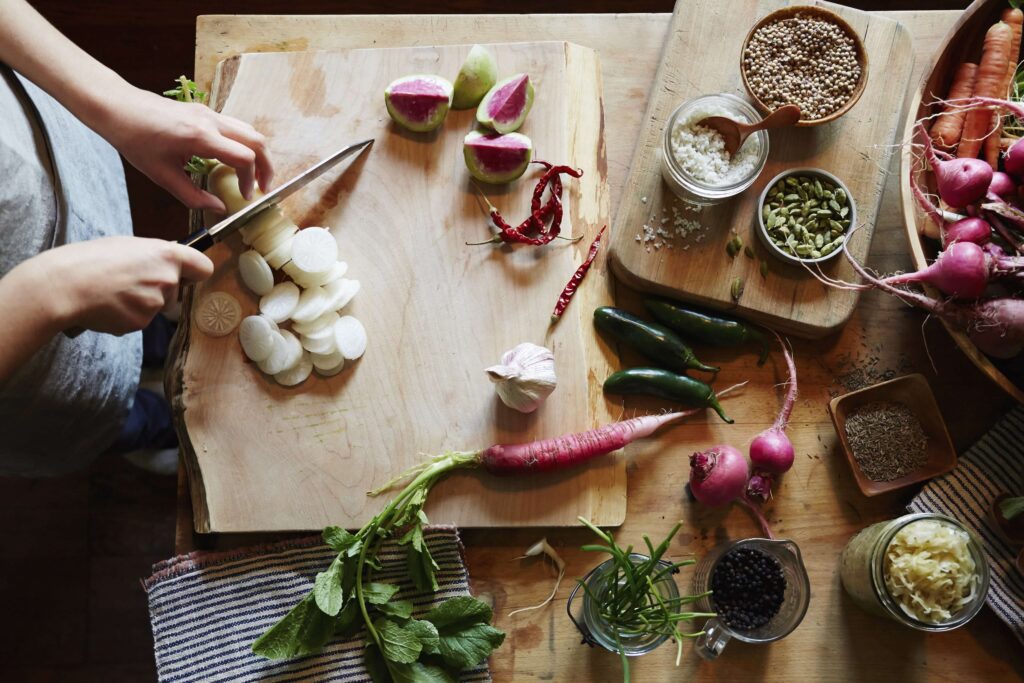 Une personne coupe des légumes sur une planche à découper placée sur une table remplie de légumes
